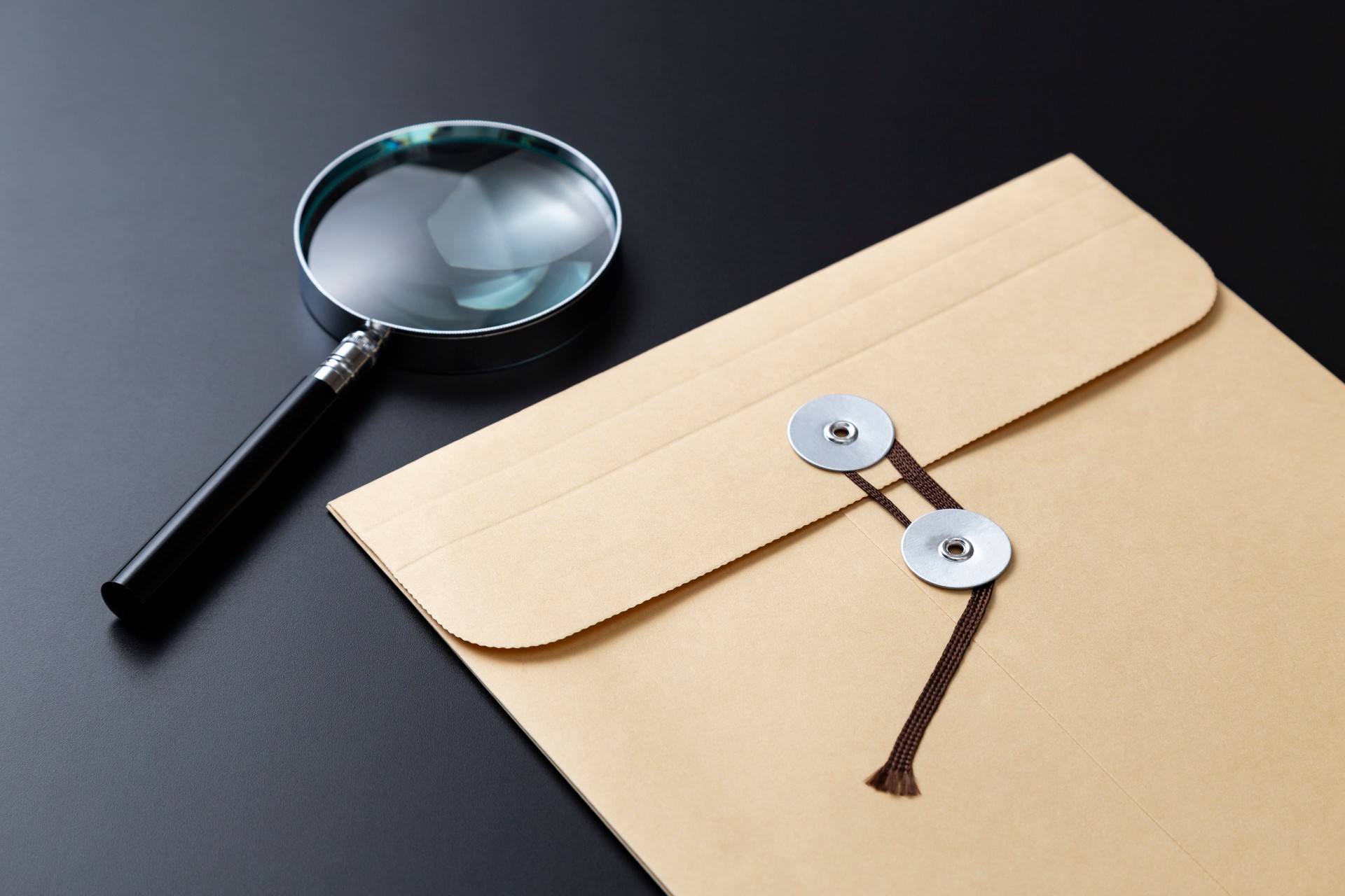 Magnifying glass and envelope with string on black background